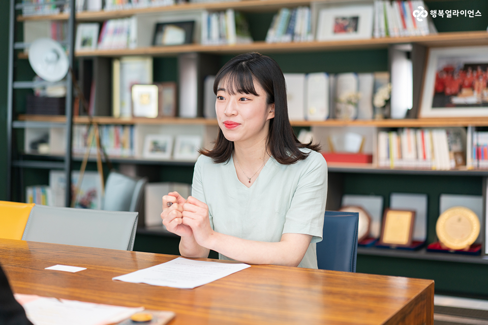 차혜인 매니저가 서가 앞에서 인터뷰어와 함께 대화를 나누고 있다. 인터뷰어는 화면에 보이지 않는다. 